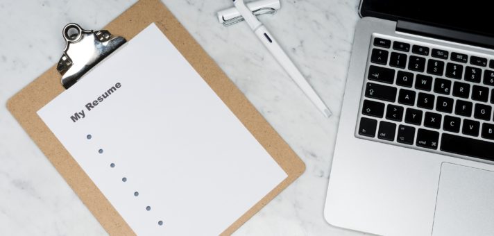 A CV or resume attached to a clipboard next to a computer on a desk