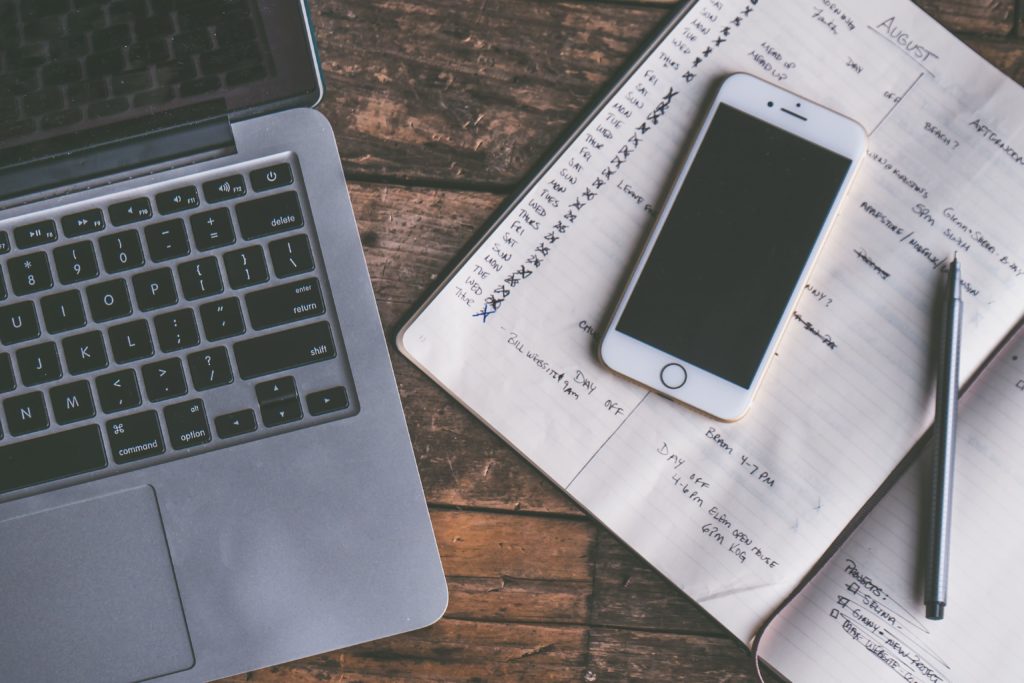 A computer, phone and notebook being used for time management